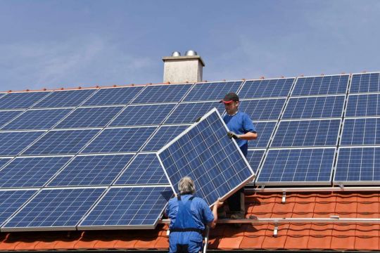 Zwei Monteure installieren eine große Photovoltaikanlage auf einem Hausdach.