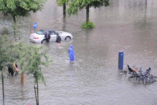Überflutete Straße in Kopenhagen, Menschen in Regensachen stehen knietief im Wasser, daneben ein Cabriolet und einige Fahrräder.