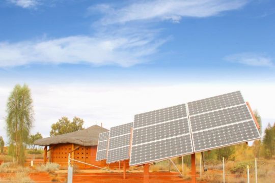 Einige aufgeständerte Solarpaneele vor einem strohgedeckten Rundhaus.