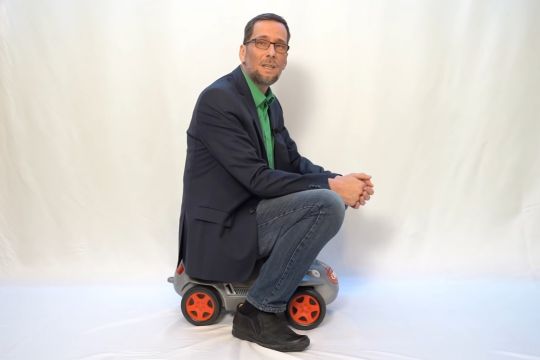 Professor Quaschning sitzt auf einem Bobbycar-Kinderauto.