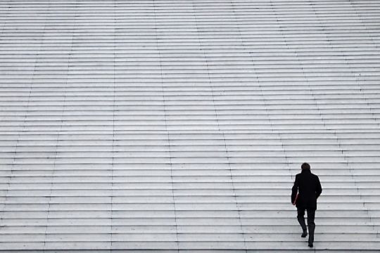 Einzelner Mann in Anzug geht allein eine riesige Treppe hinauf.