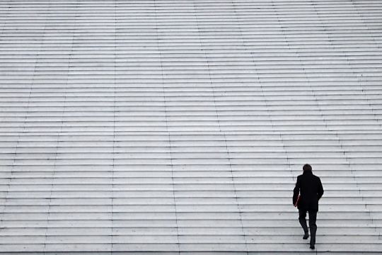 Einzelner Mann in Anzug geht allein eine riesige Treppe hinauf