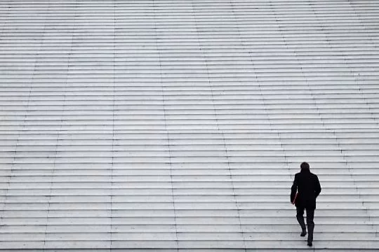 Einzelner Mann in Anzug geht allein eine riesige Treppe hinauf