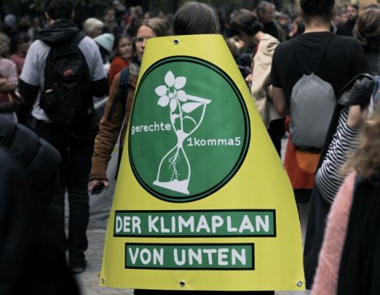 Aktivist auf einer Demo mit einem Transparent auf dem Rücken: 