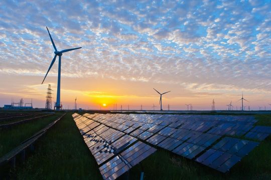 Windräder und Freiflächen-Solaranlagen vor rosa-blauem Sonnenuntergang