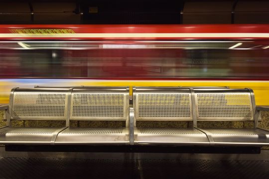 Leere Sitze auf einem U-Bahnsteig, die Bahn fährt im Hintergrund schnell vorbei.