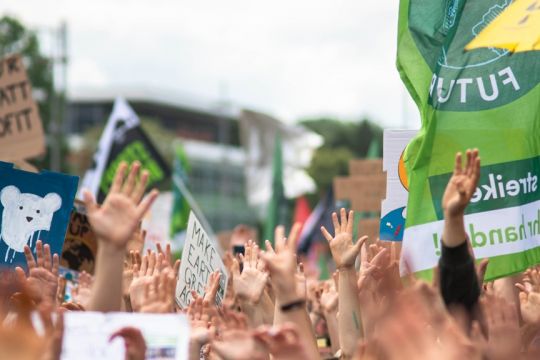 Viele in die Höhe gereckte Hände, am Rand sind selbstgemalte Demoschilder und ein Fridays-for-Future-Transparent zu sehen.