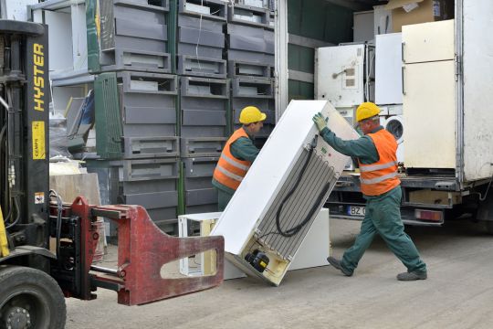 Zwei Arbeiter eines Recyclingzentrums in Bukarest laden Eisschränke von einem Lkw ab.