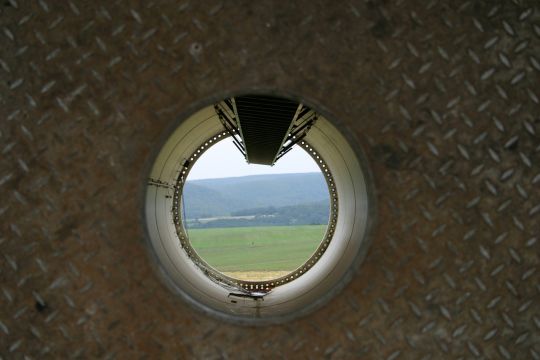 Blick durch einen liegenden Windturm: Eine Mittelgebirgslandschaft ist zu sehen. 