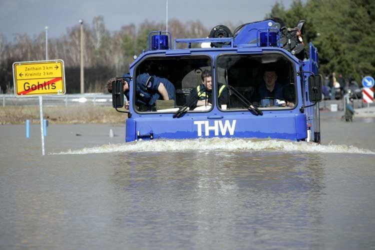 Blauer Lkw des Technischen Hilfswerks fährt durch hüfthohes Wasser.