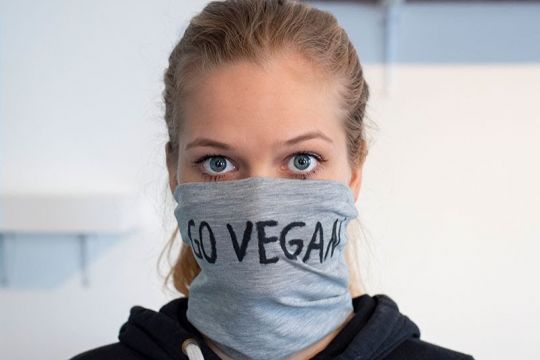 Junge Frau mit selbstgenähtem Munschutz, auf dem "go vegan" steht.