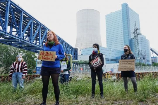 Gruppe von Aktivistinnen, teils mit Protestschildern, im Hintergrund Steinkohlekraftwerk Datteln