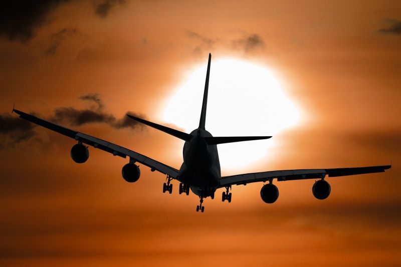 Blick von schräg unten auf ein Flugzeug, das vor einem rötlichen, etwas bewölkten Himmel in Richtung Abendsonne fliegt.