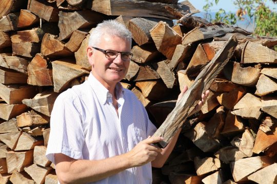 Artur Auernhammer vor einem Stapel Scheitholz.