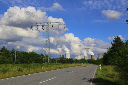 Braunkohlekoxberg Boxberg mit dampfenden Kühltürmen an einem Sommertag von der Landstraße aus betrachtet.