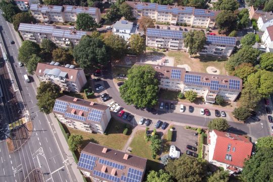 Luftaufnahme eines Wohnquartiers aus Mehrfamilienhäusern mit Solarstromanlagen auf den Dächern.