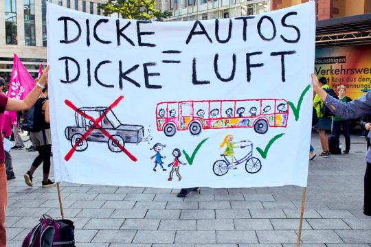 Transparent in der Fußgängerzone mit Slogan "Dicke Autos = dicke Luft" und einer großen Kinderzeichnung: Durchgestrichenes Auto – spielende, Rad und Bus fahrende Kinder.