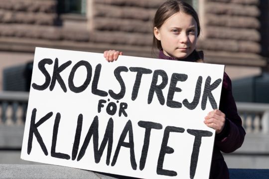Greta Thunberg hält ein weißes Schild mit der schwarzen Aufschrift 