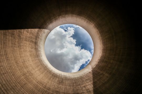 Blick aus einem betongrauen Kohlekraftwerks-Kühlturm nach oben, wo in einem Kreis der Himmel mit einer Wolke sichtbar ist. 