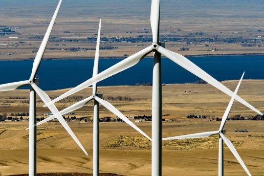 Einige Windräder in Großaufnahme vor einer kargen Landschaft mit Fluss.