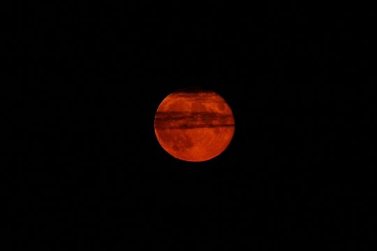 roter Mond in tiefschwarzer Nacht, davor ein faseriger schwarzer Wolkenschleier