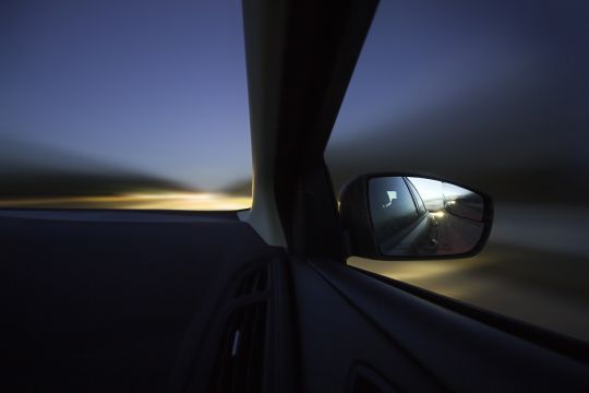 Nächtlicher Blick aus einem fahrendes Auto auf Rückspiegel und Straße.