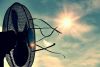 Schwarzer Ventilator, der an ihn gebundene Bänder zum fliegen bringt, vor gleißendem  Sonnenlicht