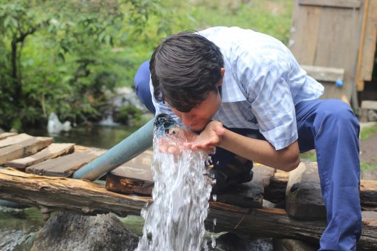 Ein Mann erfrischt sein Gesicht mit Wasser aus einem Bach.