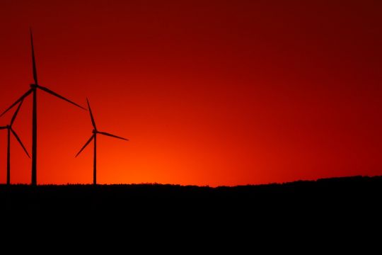 Drei Windräder am Horizont vor tiefrotem Abendhimmel.