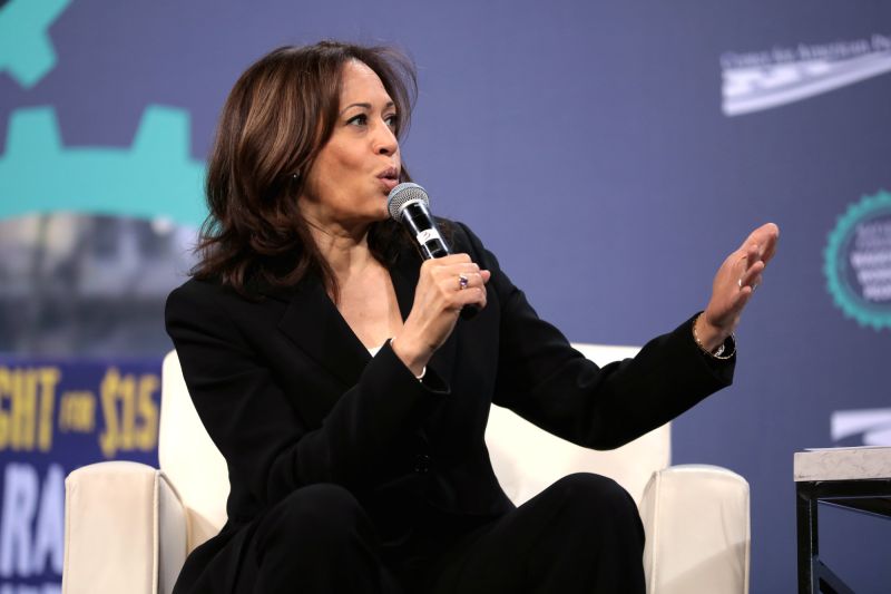 Kamala Harris sitzt auf der Bühne, spricht ins Mikro und unterstreicht das Gesagte mit einer ausladenden Hand-Geste.