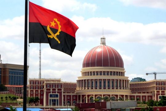 Parlamentsgebäude in Luanda mit weinroter Kuppel, im Vordergrund die rot-schwarze Flagge Angolas.