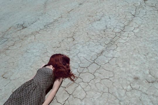 Eine junge Frau liegt auf rissigem Boden.
