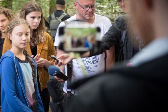 Greta Thunberg und Luisa Neubauer stehen mit ernstem Gesichtsausdruck und von Kameras umringt uf einer Lichtung.