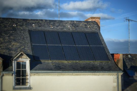 Solarpaneele auf dem Dach eines kleineren, älteren Hauses.