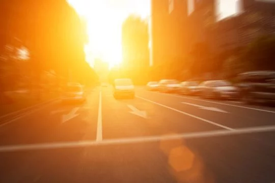 Sonnenuntergang am Ende einer mehrspurigen, von Gebäuden gesäumten Hauptstraße voller Autos. 