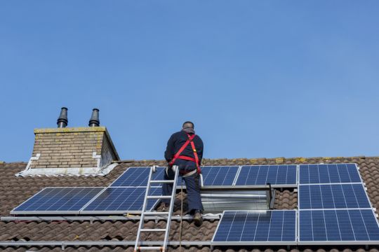 Ein Monteur ist mit der Installation einiger Solarmodule auf einem Hausdach beschäftigt.