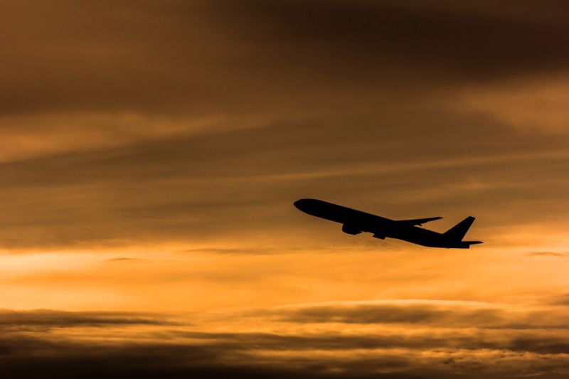 Silhouette eines startenden Flugzeugs vor gelblichem Abendhimmel.
