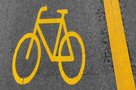 Gelbes Fahrradsymbol und gelber Streifen auf Asphalt.