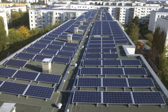 Viele Photovoltaikpaneele auf dem Flachdach eines Plattenbau-Hochhauses im Osten Berlins.