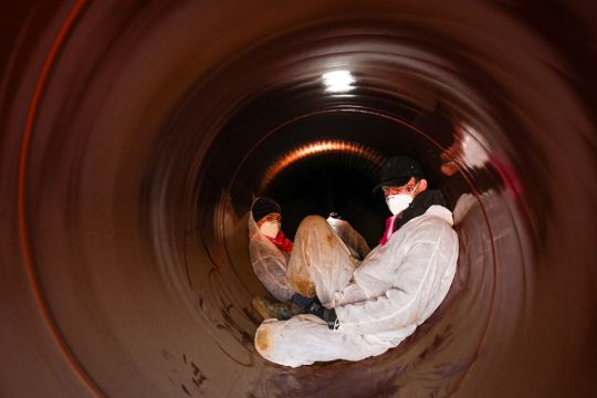 Zwei weiß gekleidete Klimaaktivisten sitzen in einer im Bau befindlichen Erdgaspipeline.