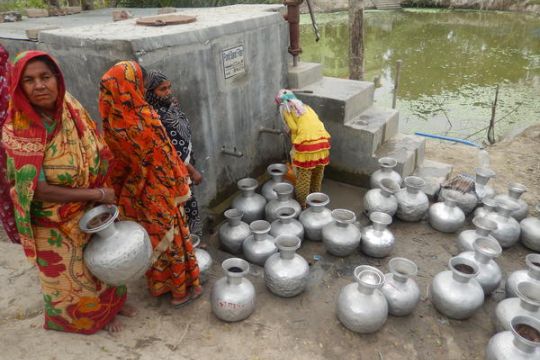 Einige Frauen mit vielen Metallkannen vor einem Trinkwasserbrunnen im Süden von Bangladesch.