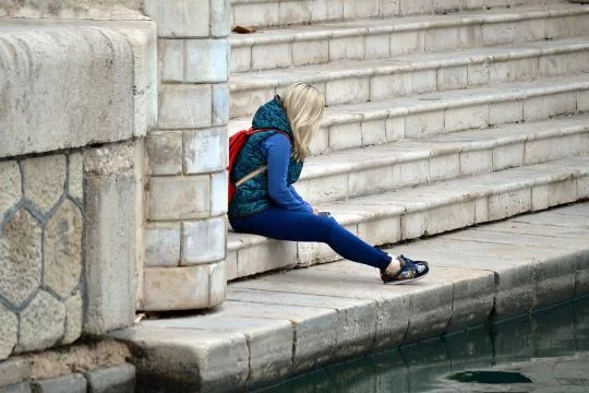 Junge Frau sitzt allein mit abgewendetem Blick auf einer Treppe