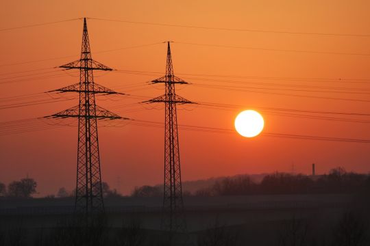 Zwei Strommasten in der Abenddämmerung vor untergehender Sonne.