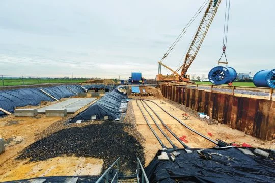 Ein Kran legt Kabeltrommeln neben der ausgeschachteten Fläche einer Erdkabelbaustelle ab.