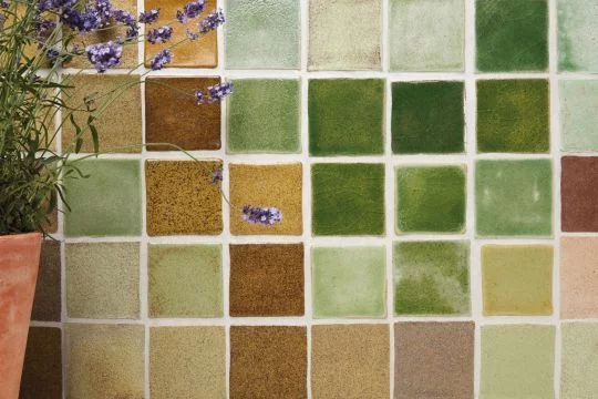 Wand mit verschiedenen Recyclingfliesen in angenehmen Tönen, am Rand steht ein Blumentopf mit Lavendel.