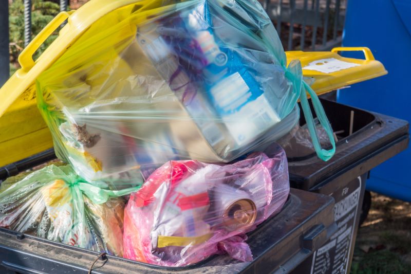 Offene Mülltonne mit gelbem Deckel, Säcke voller Plastikmüll sind hineingestopft.