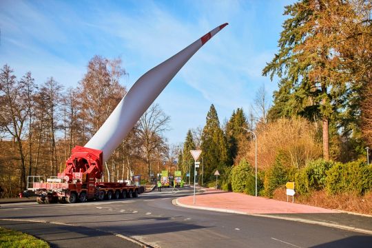 Ein selbstfahrender Auflieger transportiert ein schräg nach oben weisendes Windrad-Rotorblatt über die Landstraße von Heinzenberg nach Weilmünster.