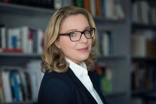 Claudia Kemfert vor verschwommener Bücherwand.