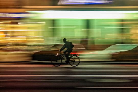 Nachts auf einer breiten Stadtstraße fährt ein Radfahrer.