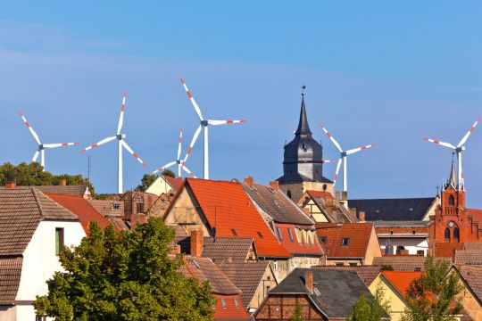 Blick über die Dächer einer Kleinstadt, im Hintergrund einige Windräder.